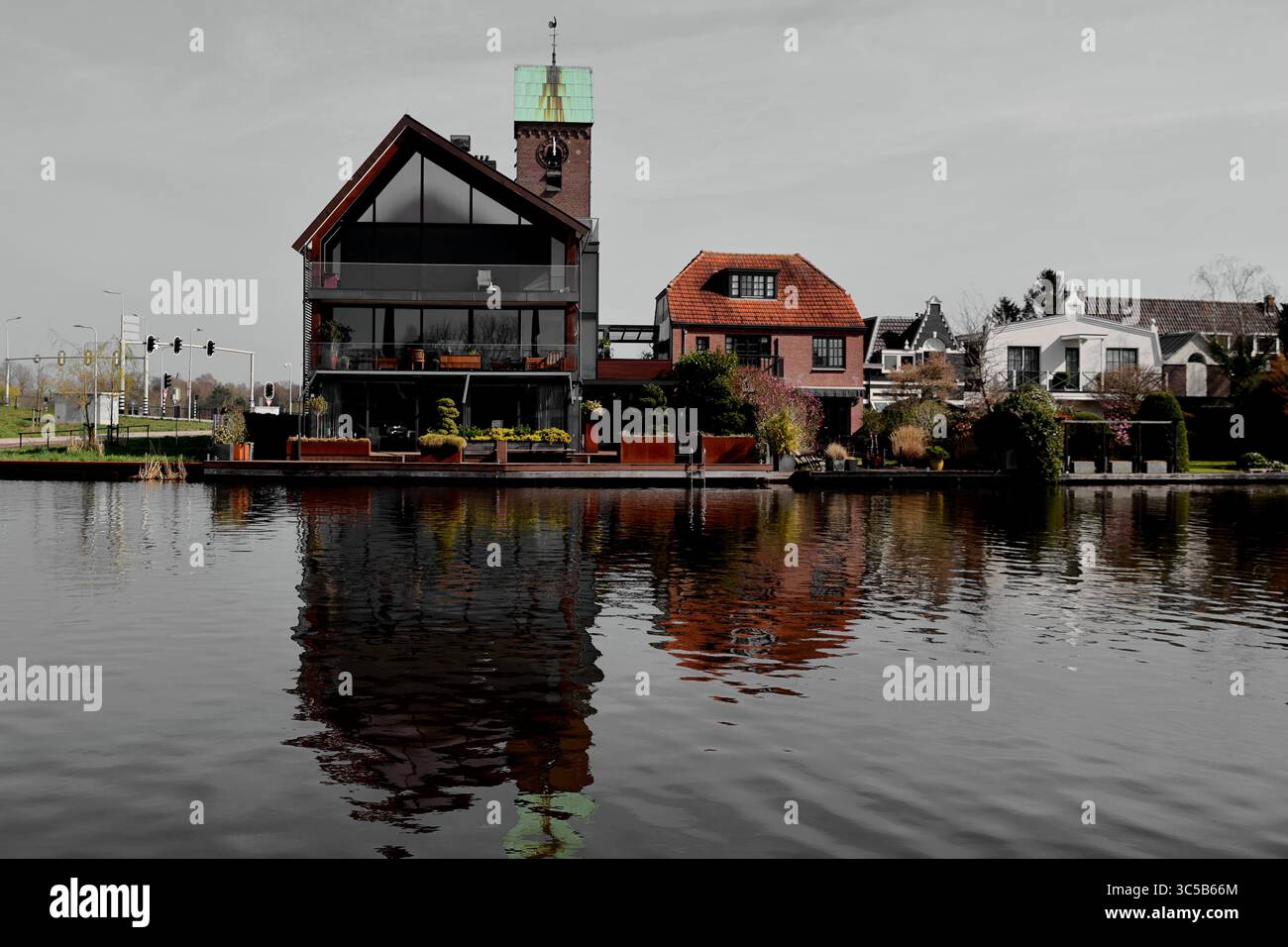 Amstelzijde in Ouderkerk aan de Amstel bietet moderne und malerische Häuser, die sich in ruhigem Wasser unter hellem Himmel spiegeln und die ruhige Harmonie am Fluss einfangen. Stockfoto