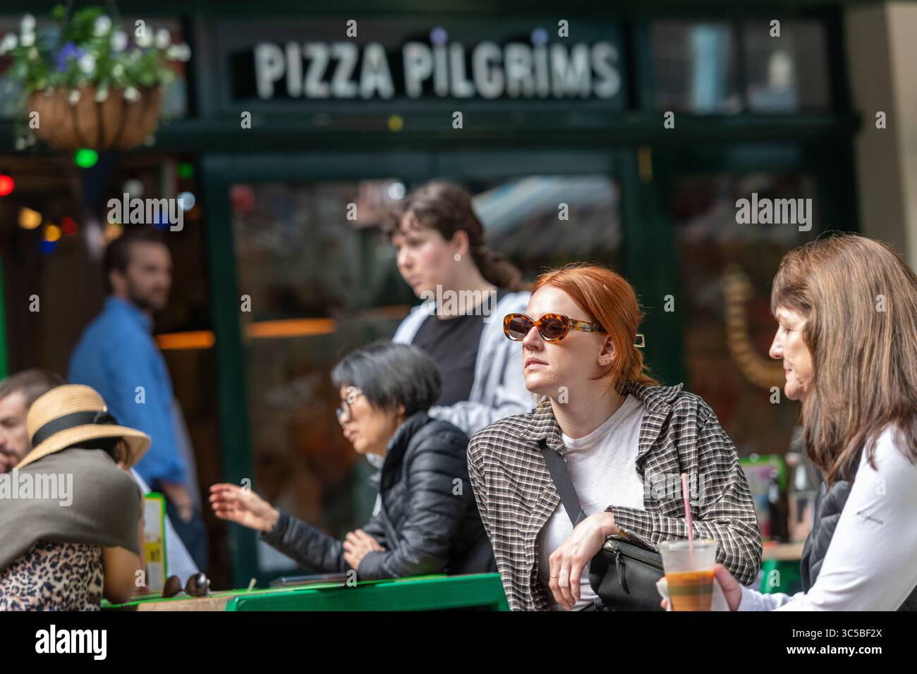 Die Gäste speisen an einem sonnigen Tag außerhalb der Pizza Pilgrims in Kingly Court, Soho, London, und halten den urbanen Lebensstil und die ungezwungene Esskultur in der Stadt fest. Stockfoto