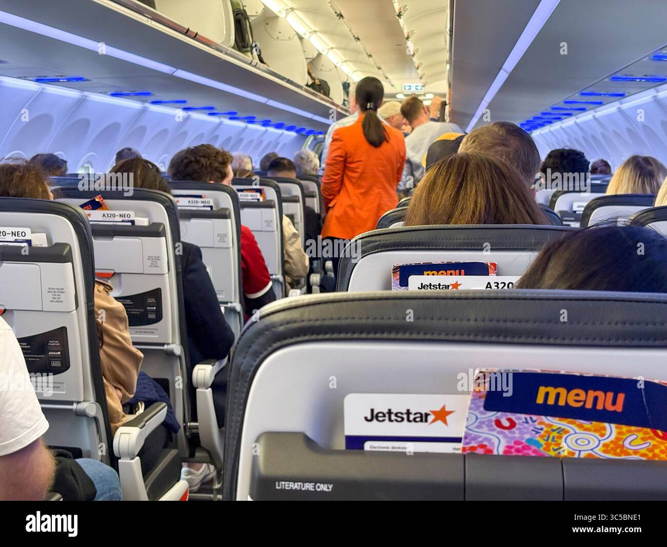 Jetstar-Flug von Sydney nach Melbourne mit dem Airbus A320 NEO sitzen Passagiere in Flugzeugen, wobei die Stewardess-Flugbegleiterin anderen Passagieren hilft Stockfoto
