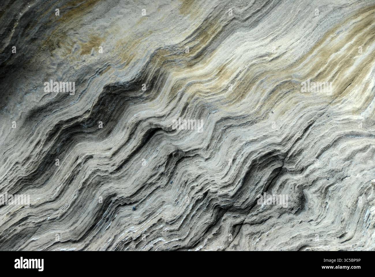Nahaufnahme von geschichteten vulkanischen Gesteinsformationen mit welligen Sedimentmustern, die komplexe natürliche Texturen und geologische Details im Freien zeigen Stockfoto