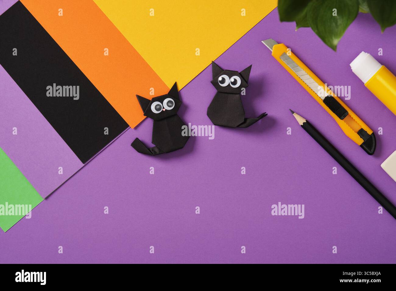 Papier-Origami-schwarze Katzen mit geschwollenen Augen auf violettem Hintergrund. Rund um Bastelbedarf, Papierbögen, Bleistift, Radiergummi, Kleber und Messer für Heimwerkerprojekte Stockfoto