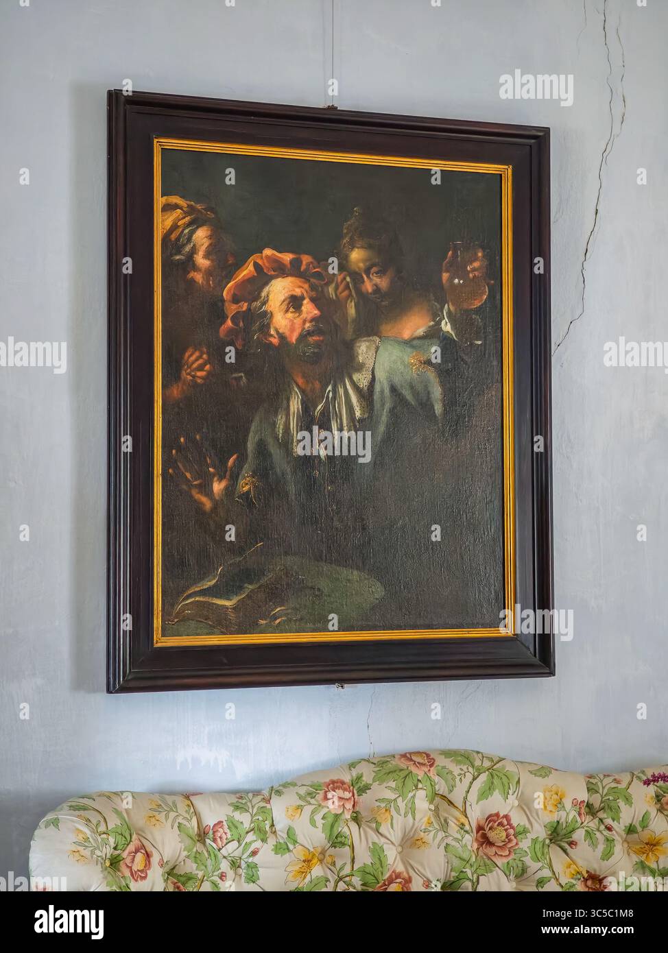Nahaufnahme eines alten Ölgemäldes mit expressiven Figuren in dramatischer Beleuchtung, montiert an einer Wand über einem floralen Vintage-Sofa in einem historischen Inter Stockfoto