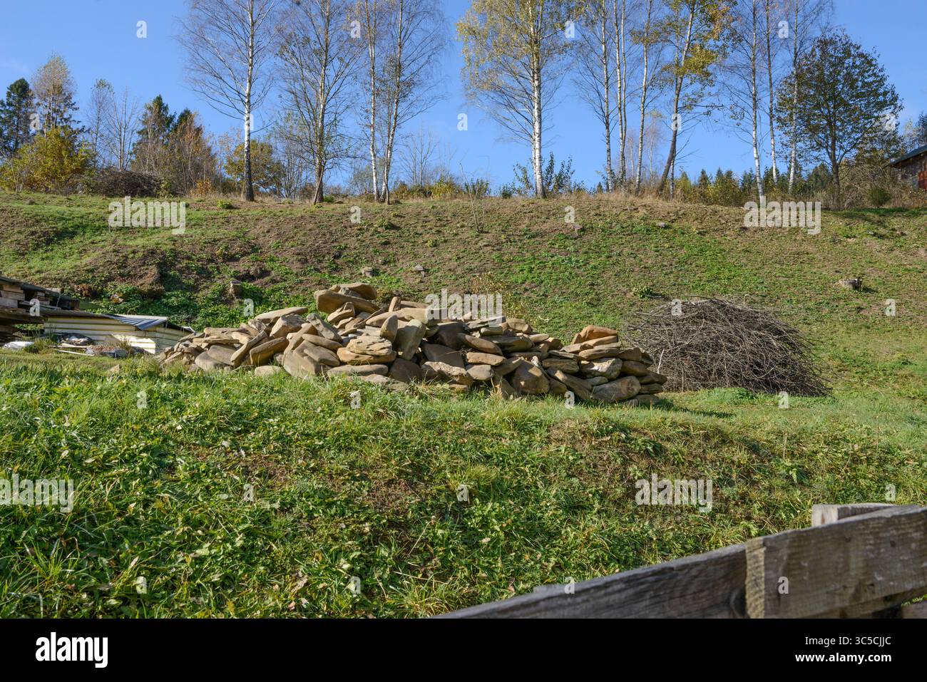 Großabhang des Hinterhofhügels mit Haufen flacher Steine und Reisig auf grünem Gras in Skhidnytsia, Westukraine. Stockfoto