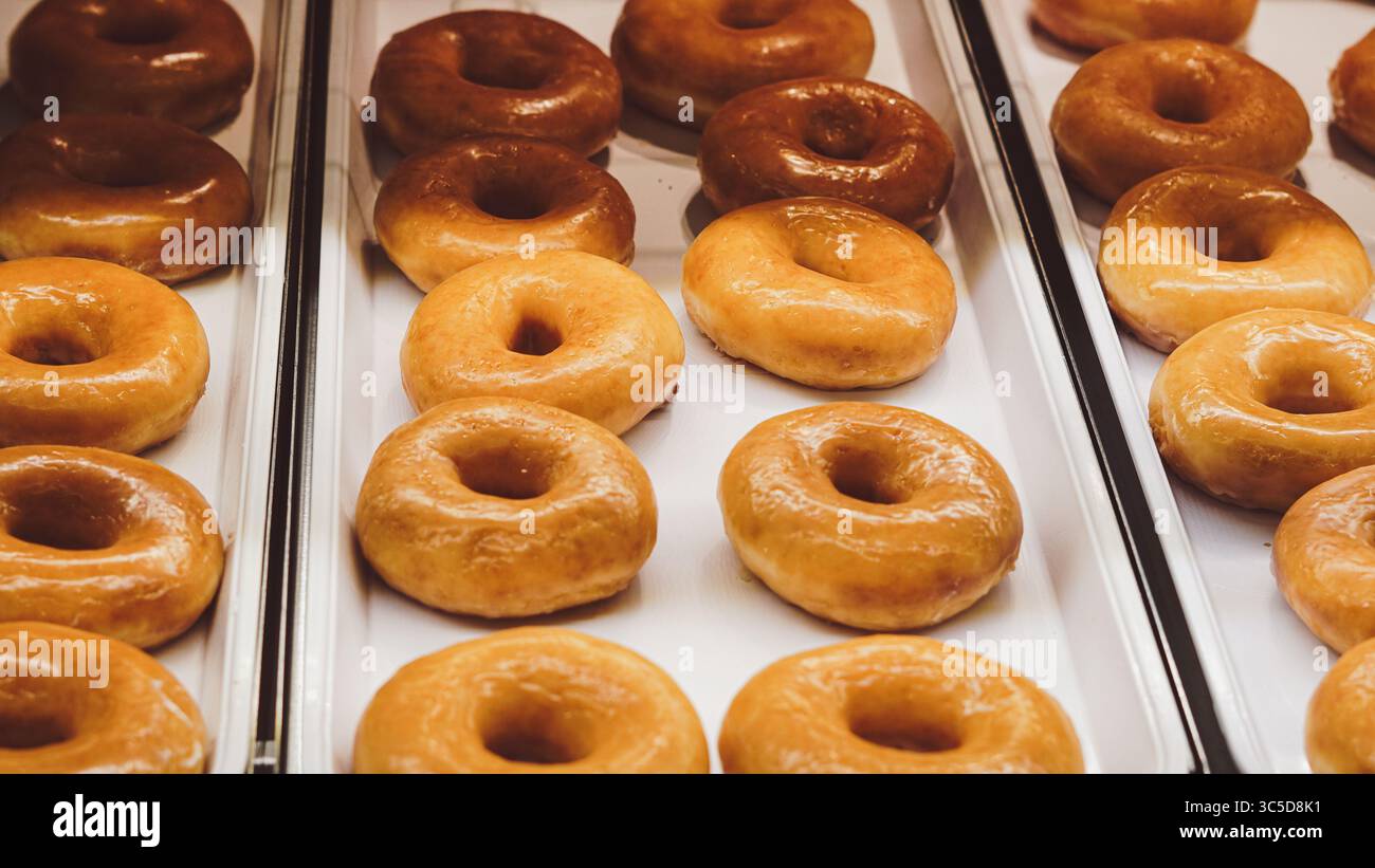 Verschiedene glasierte Donuts hinter Backglas im Fenster des Cafés Stockfoto