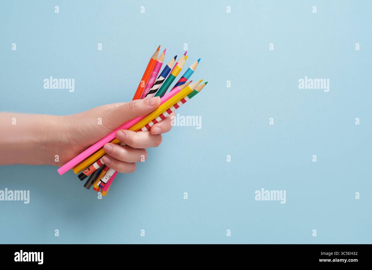 Die Hand hält farbige Bleistifte auf hellblauem Hintergrund aus Stockfoto