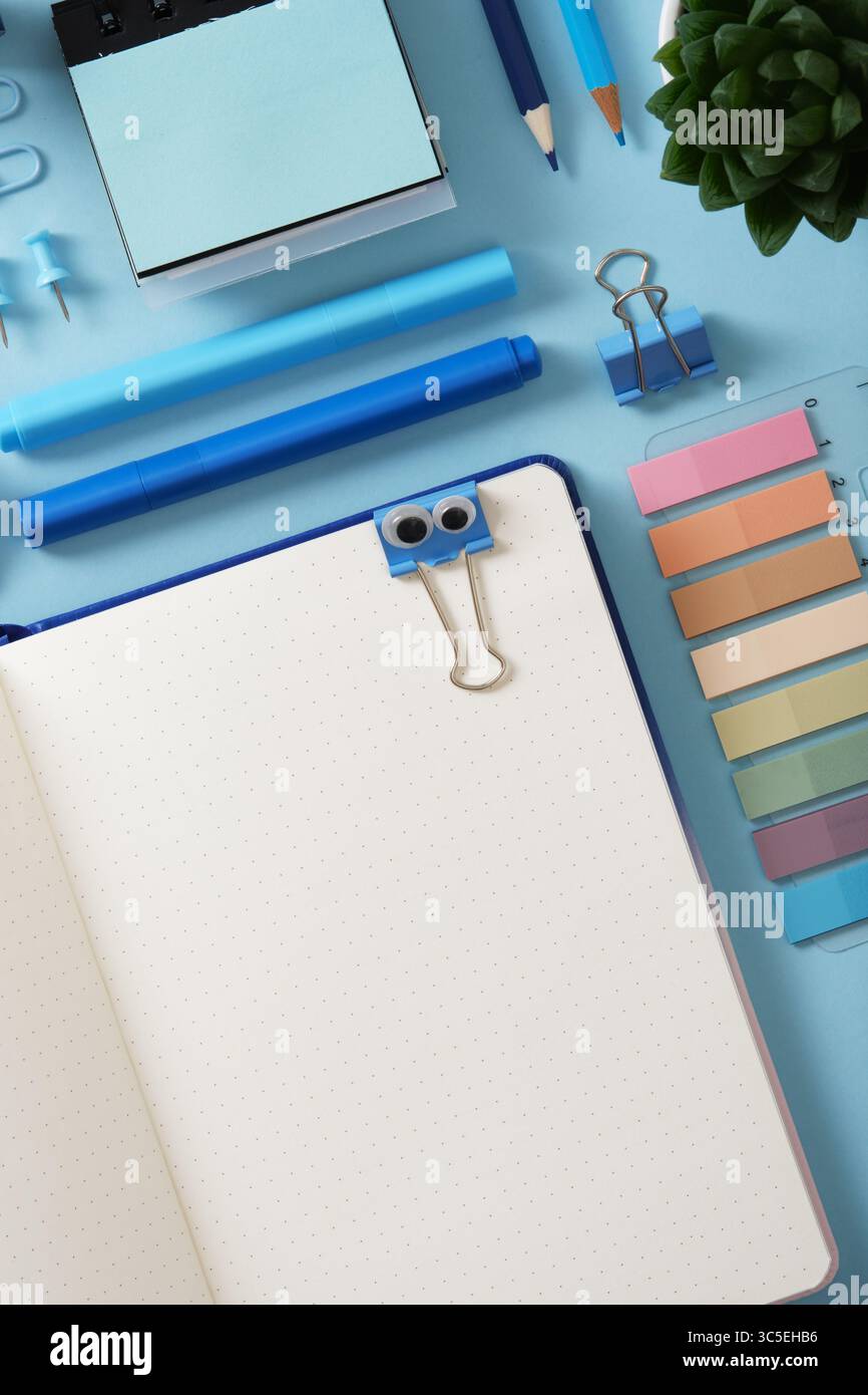 Blick von oben auf den Schreibtisch mit blauem Schreibpapier. Lustige Büroklammer mit Augen wird an einem offenen Notizblock befestigt. Kopierraum. Stockfoto