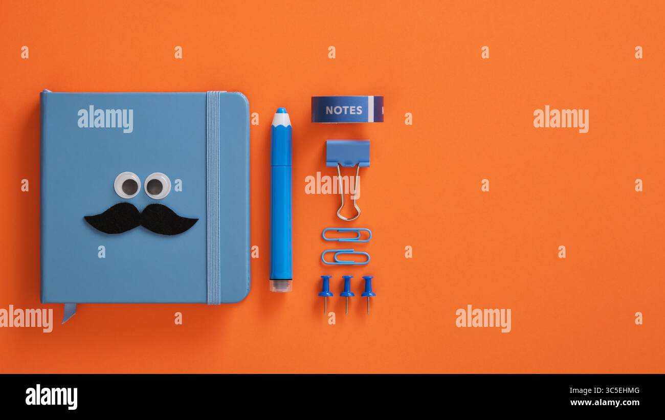 Blauer Notizblock mit guten Augen und Schnurrbart und Briefpapier auf einem leuchtend orangen Hintergrund. Kopierraum. Stockfoto