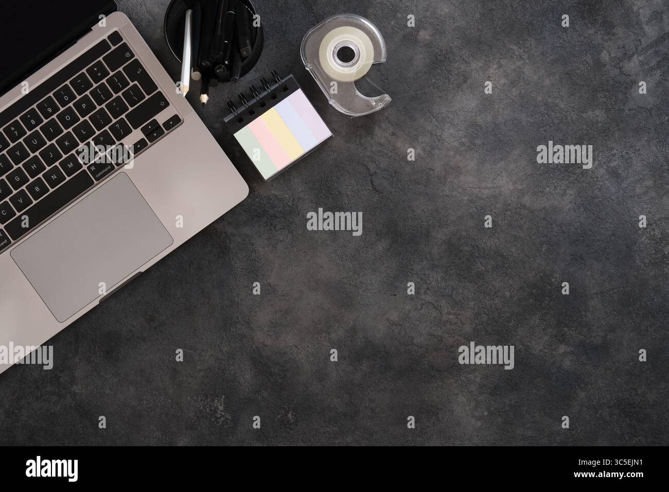 Minimalistischer Schreibtisch mit Laptop, Klebeband, Stift auf dunklem strukturiertem Hintergrund. Platzieren für Ihren Text. Stockfoto