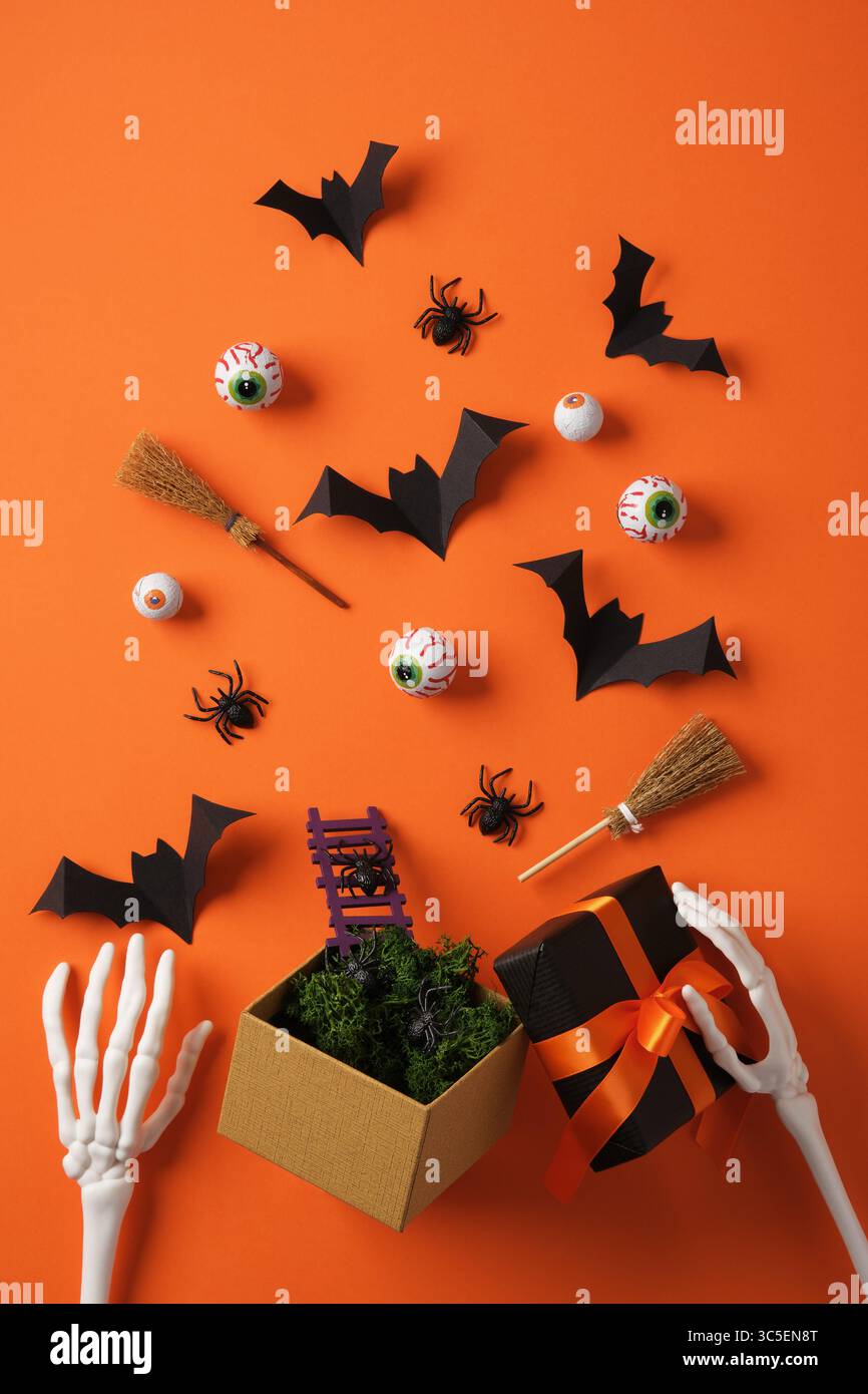 Fledermäuse fliegen aus der Geschenkbox, Spinnen kommen, Augen Rollen aus. Gruselige Halloween-Dekorationen und Accessoires auf orangem Hintergrund. Stockfoto