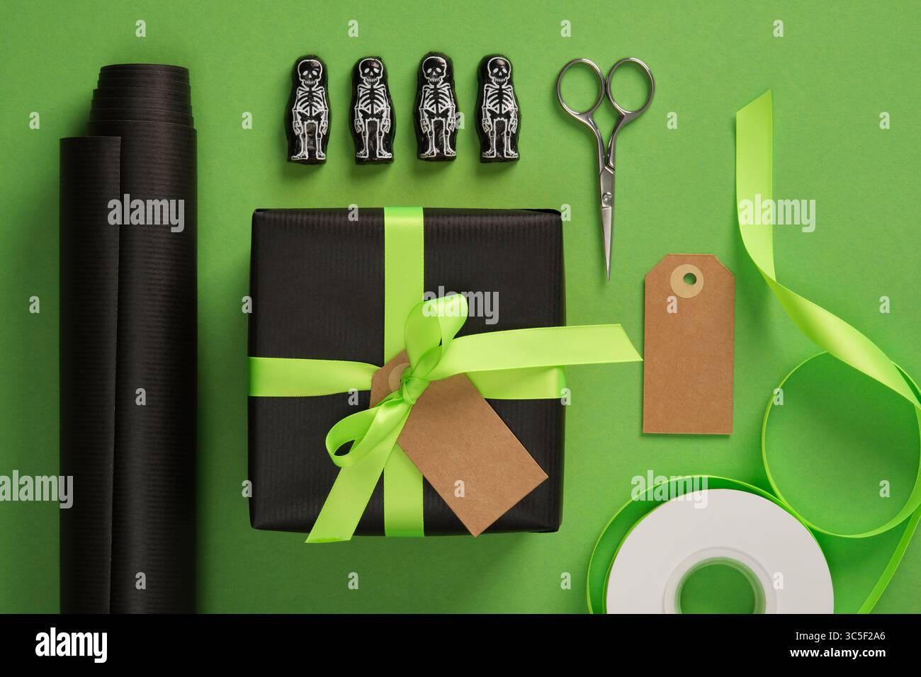 Halloween Geschenkverpackung mit Skelettfiguren, schwarzem Papier und neongrünem Band auf grünem Hintergrund. Urlaubsvorbereitung. Stockfoto