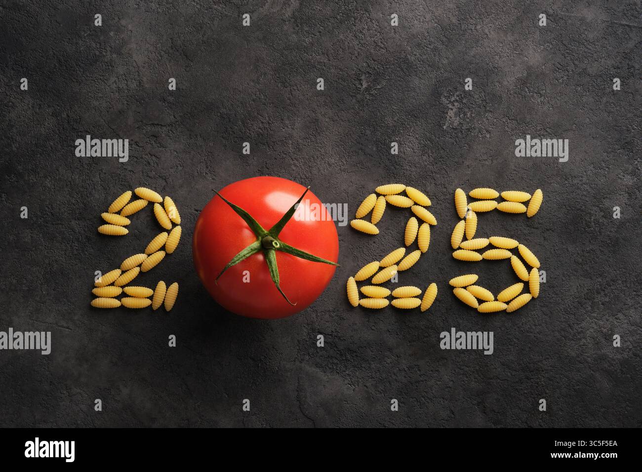 2025 kulinarische Kunst mit Tomaten und Nudeln auf dunklem Steinhintergrund. Kreatives kulinarisches Design für das neue Jahr. Stockfoto