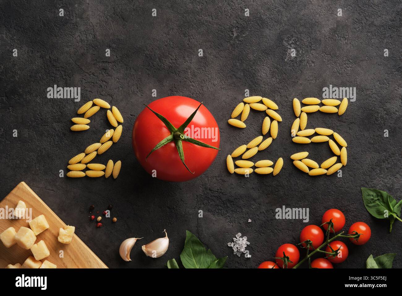 Das Jahr 2025 ist mit Tomaten und Nudeln auf dunklem Steingrund gesäumt. Ein kulinarisches Design für das neue Jahr. Stockfoto