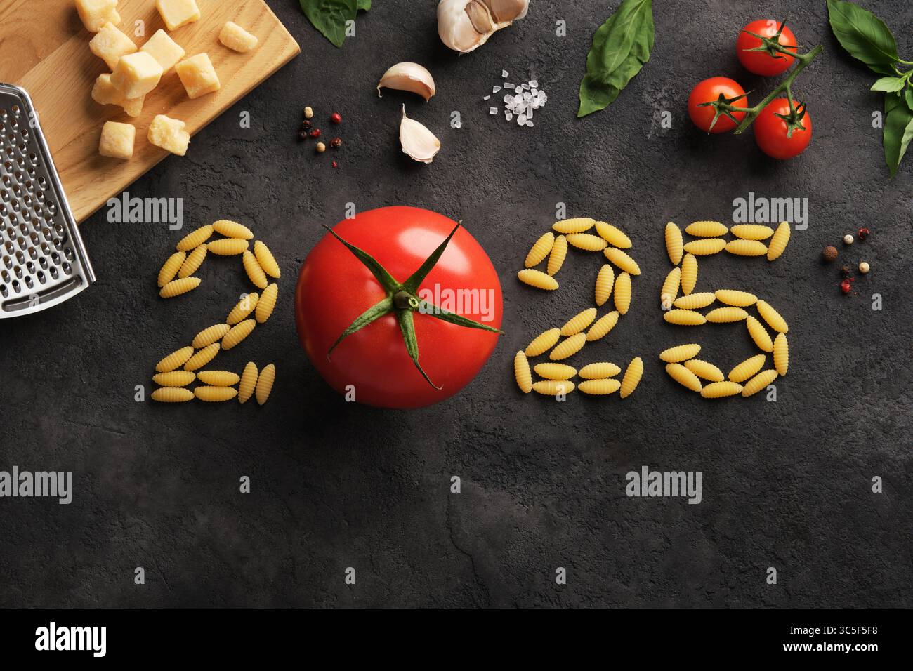 Zahlen 2025 aus Nudeln und Tomaten auf dunklem Steinhintergrund. Eine kulinarische Idee für das neue Jahr. Stockfoto