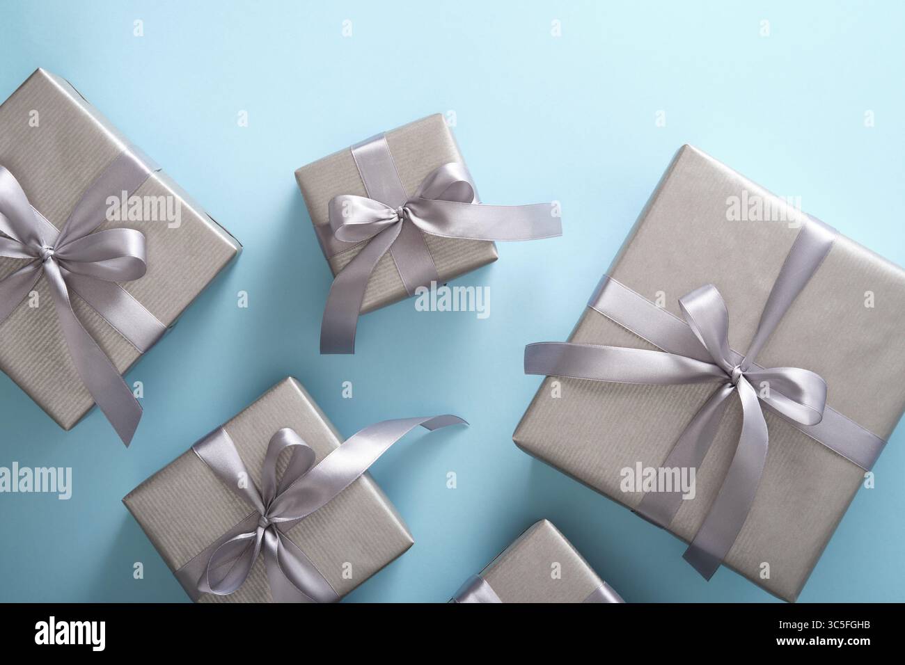 Set aus einfarbigen silbernen Geschenkboxen mit grauen Bändern auf hellblauem Hintergrund. Stockfoto