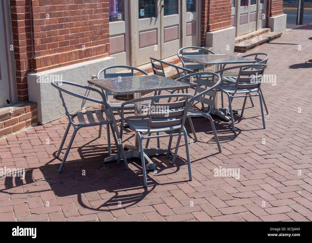 Metalltische und -Stühle im Freien auf einer sonnigen Terrasse im Straßencafé. Stockfoto