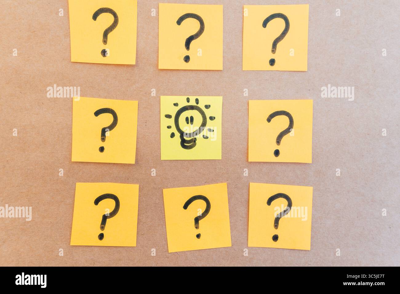 Beleuchteter Scheinwerfer, umgeben von Fragezeichen, die auf farbigem Papier mit schwarzem Marker mit einheitlichem, solidem Hintergrund gezeichnet sind Stockfoto
