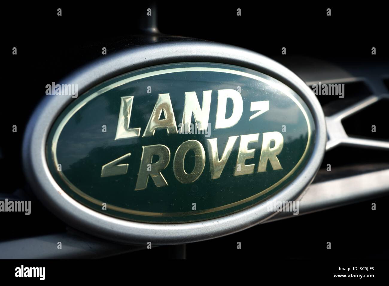 Land Rover Emblem in Grün und Gold auf einem Kühlergrill mit silberner Verkleidung und dunklem Hintergrund. Stockfoto
