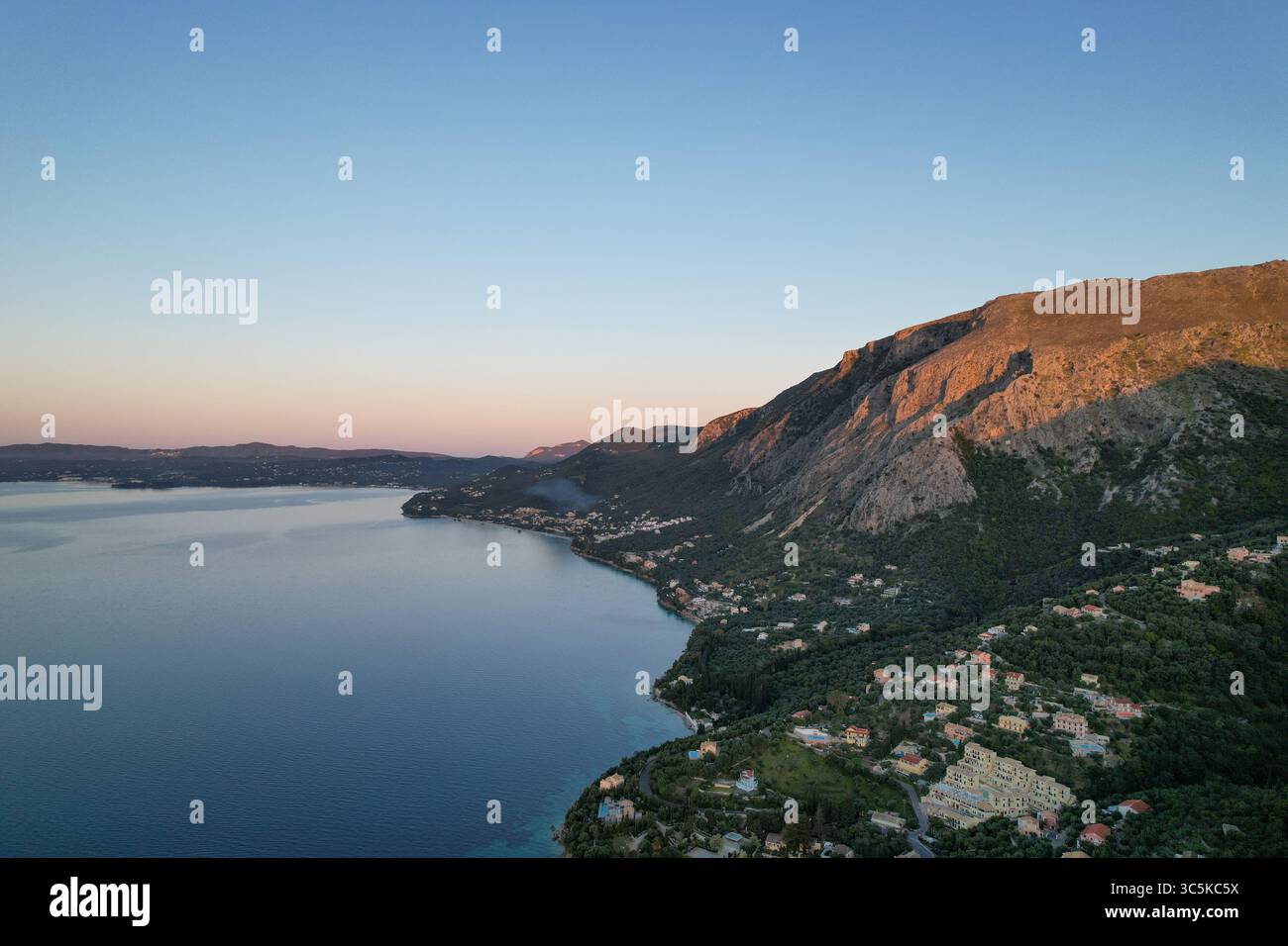 Aus der Vogelperspektive auf die Küste, wo das Land unter einem sanften Sonnenschein auf das Ionische Meer trifft, Korfu, Griechenland. Stockfoto