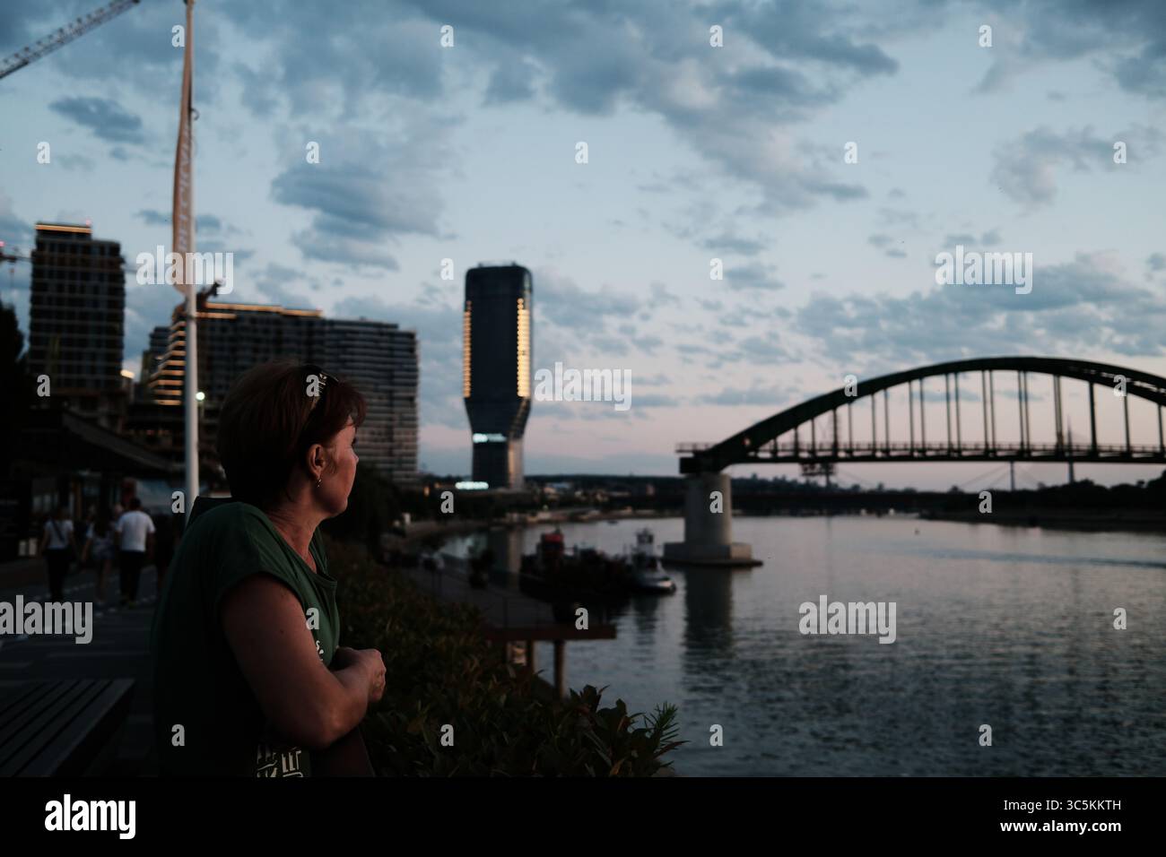 Frau genießt die Aussicht bei Sonnenuntergang an der Save in Belgrad, Serbien. Moderne Belgrader Hafengebäude und die alte Brücke bilden einen Kontrast zum alten Stockfoto