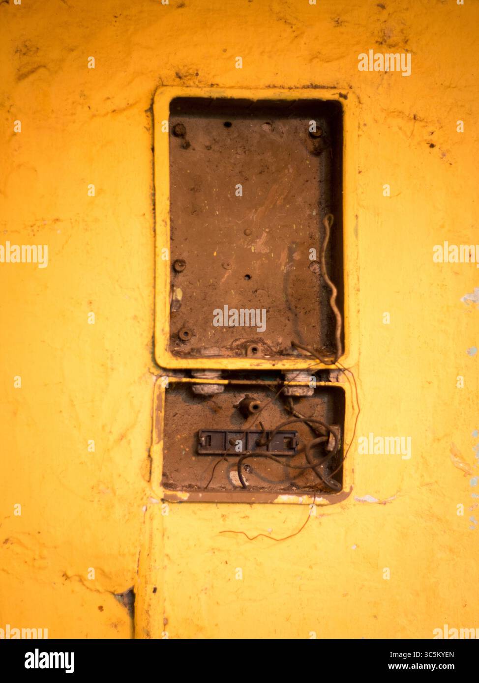 Defekter Schaltkasten an der gelben Wand. Stockfoto