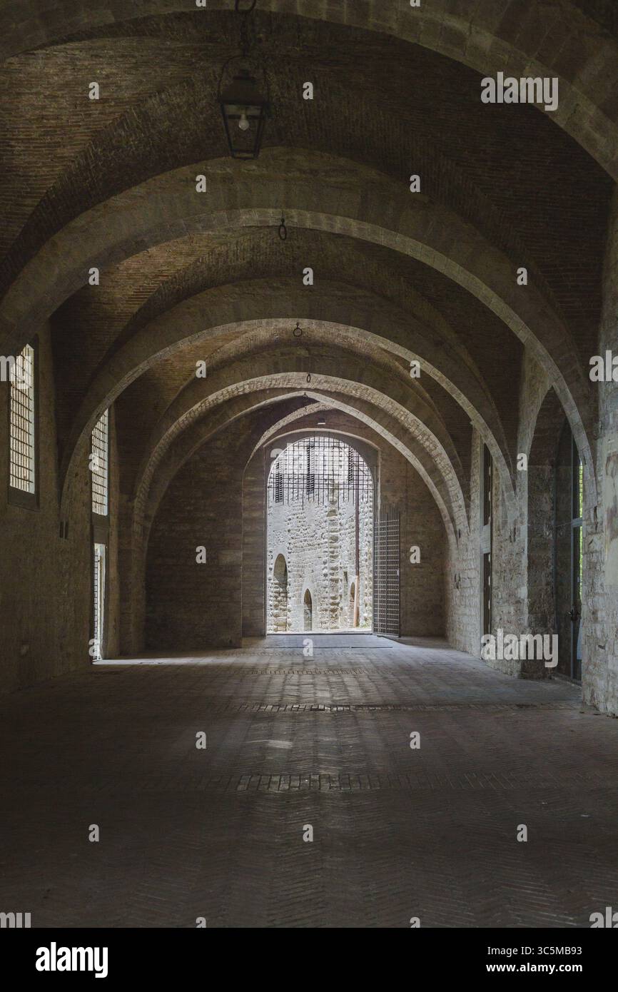 Blick auf Steinbögen, die lange Schatten werfen, führt zu einer hell beleuchteten Öffnung in einem alten Gebäude, einer zeitlosen Szene von architektonischer Schönheit, Gubbio, Umbrien, Italien. Stockfoto