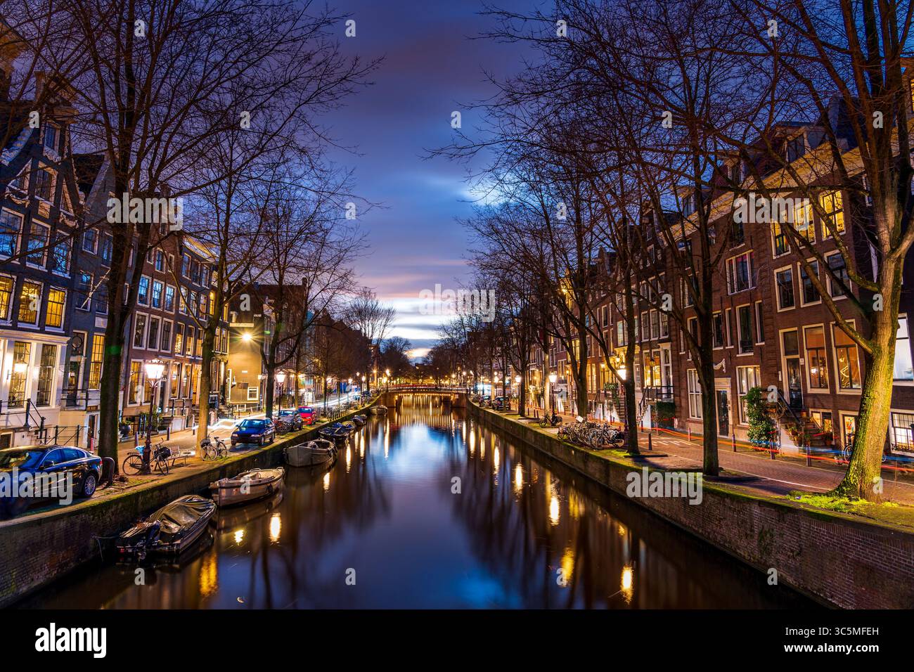Die berühmten Tanzhäuser von Damrak, wunderschön beleuchtet und reflektiert auf dem ruhigen Kanalwasser, schaffen eine magische Szene im Herzen von AMS Stockfoto