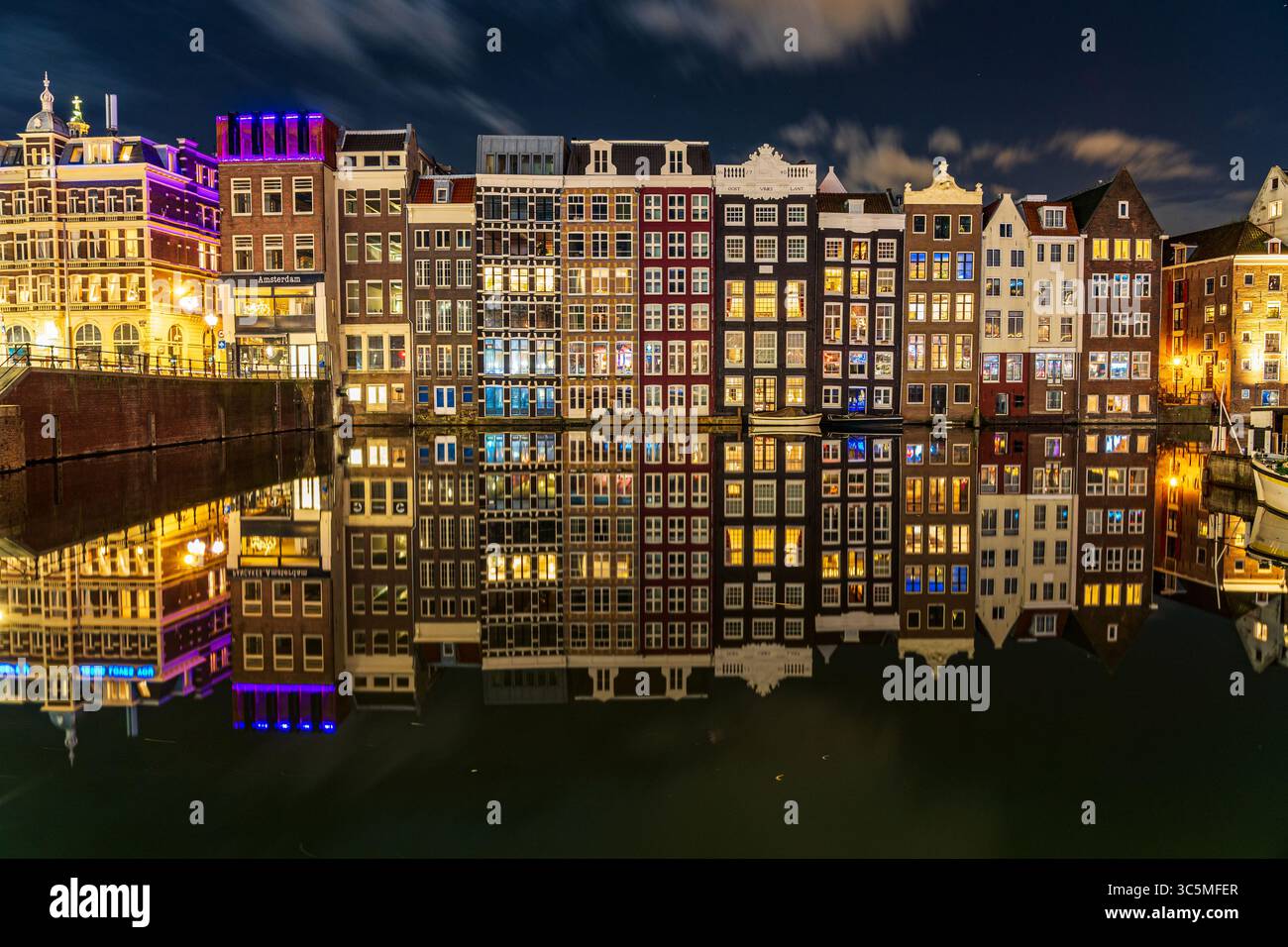 Die berühmten Tanzhäuser von Damrak, wunderschön beleuchtet und reflektiert auf dem ruhigen Kanalwasser, schaffen eine magische Szene im Herzen von AMS Stockfoto