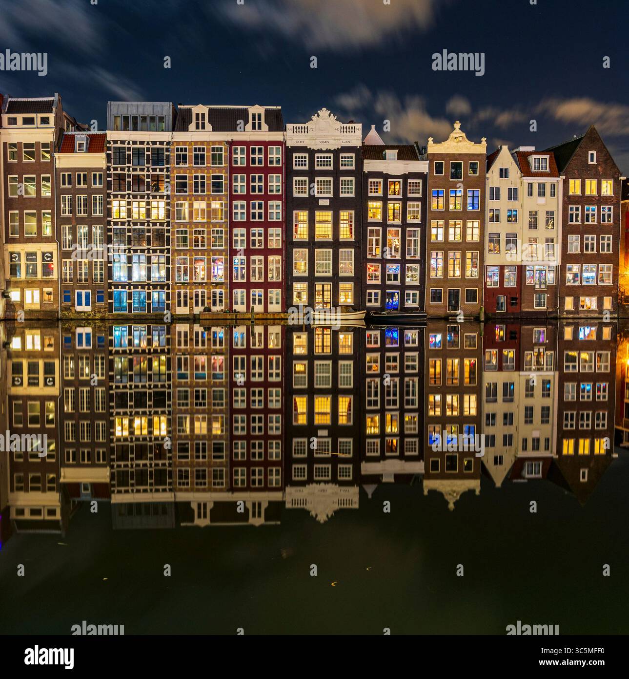 Die berühmten Tanzhäuser von Damrak, wunderschön beleuchtet und reflektiert auf dem ruhigen Kanalwasser, schaffen eine magische Szene im Herzen von AMS Stockfoto