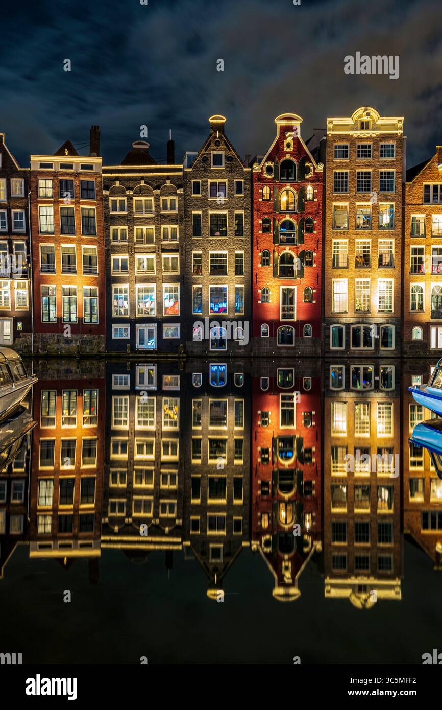 Die berühmten Tanzhäuser von Damrak, wunderschön beleuchtet und reflektiert auf dem ruhigen Kanalwasser, schaffen eine magische Szene im Herzen von AMS Stockfoto