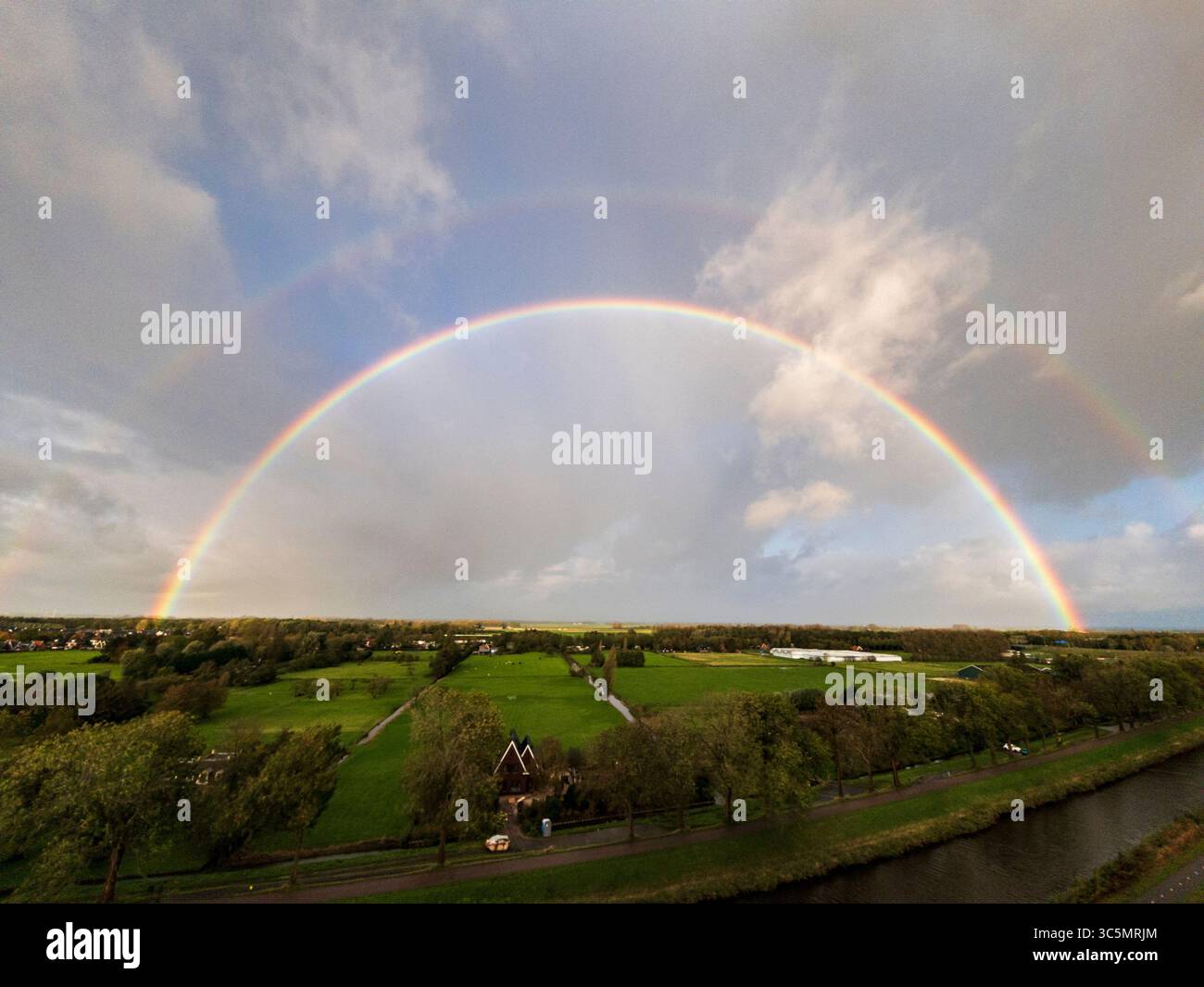 Atemberaubender Balkonblick auf einen Regenbogen über Purmerends Landschaft bei einem stürmischen Sommeruntergang in der Nähe von Amsterdam, Niederlande Stockfoto