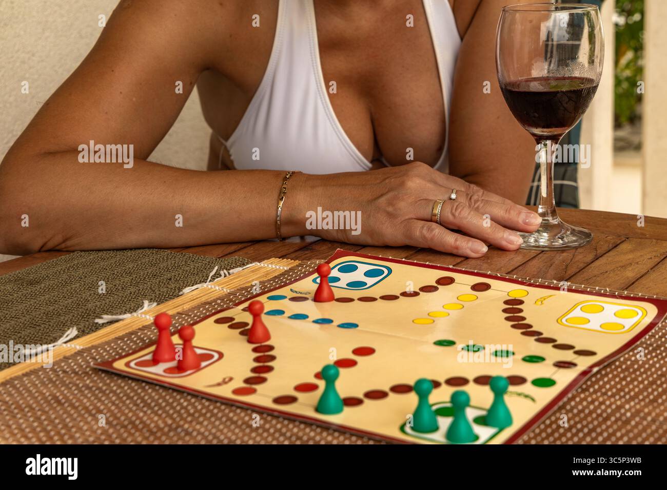 Eine Frau mit einem Glas Rotwein sitzt an einem Tisch und spielt ein Brettspiel, spielt chinesische Schachfiguren, eine Möglichkeit, Freizeit im Urlaub zu verbringen Stockfoto