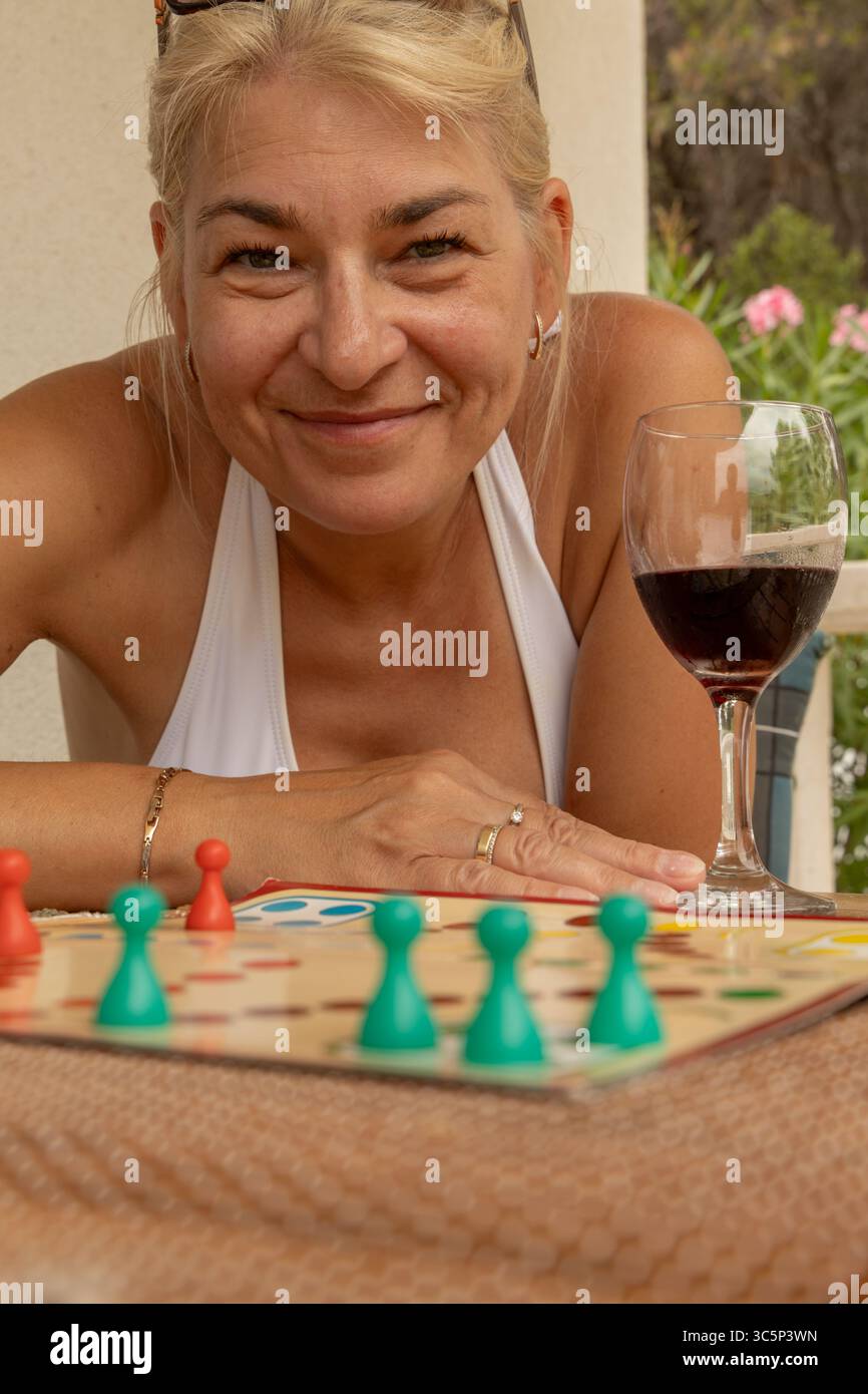 Eine Frau mit einem Glas Rotwein sitzt an einem Tisch und spielt ein Brettspiel, spielt chinesische Schachfiguren, eine Möglichkeit, Freizeit im Urlaub zu verbringen Stockfoto