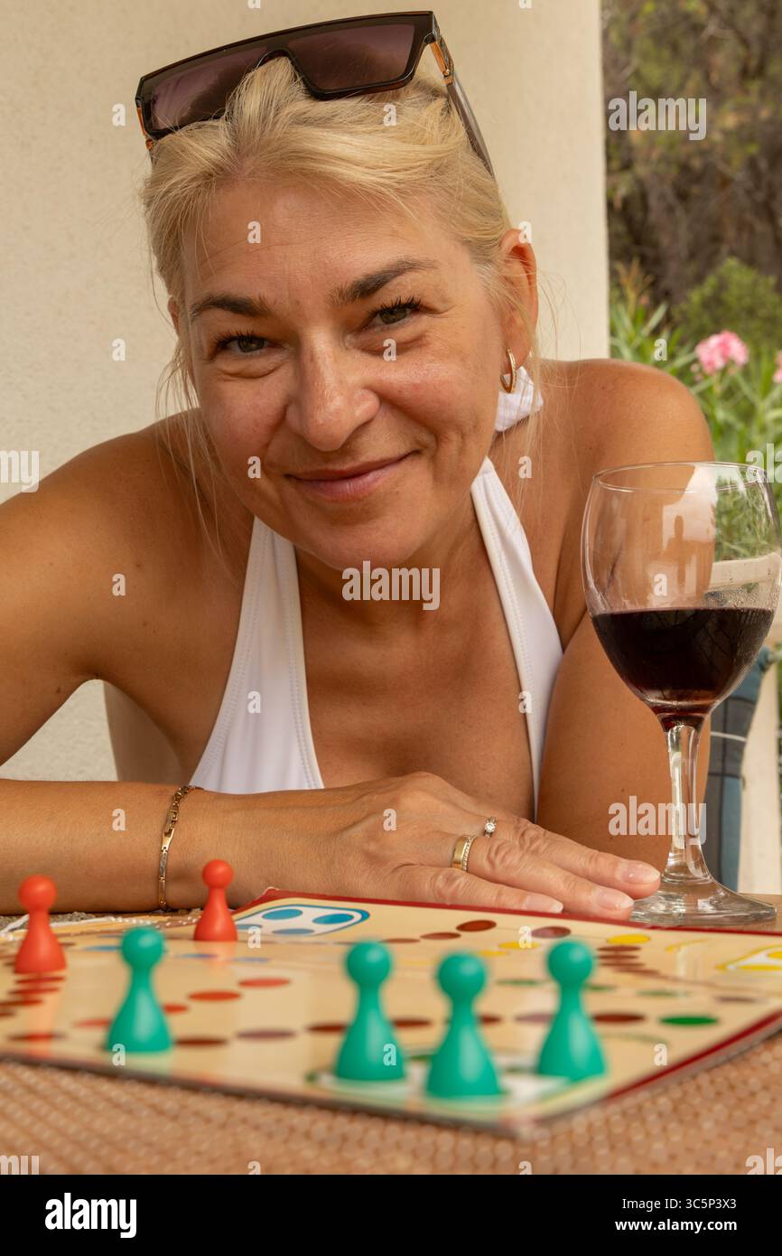 Eine Frau mit einem Glas Rotwein sitzt an einem Tisch und spielt ein Brettspiel, spielt chinesische Schachfiguren, eine Möglichkeit, Freizeit im Urlaub zu verbringen Stockfoto