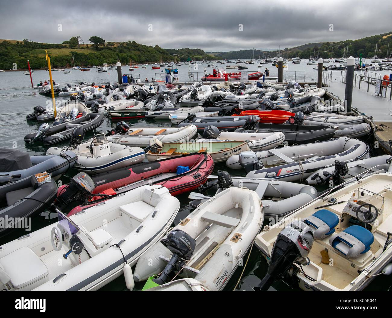Zahlreiche aufblasbare Boote vertäuten in einem geschäftigen Yachthafen vor einem Hintergrund von üppigem Grün und stimmungsvollem Himmel Salcombe Hafen/Hafen eng zusammen Stockfoto