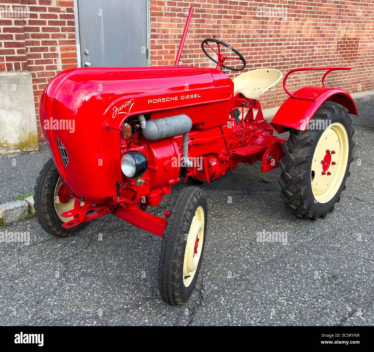 Whippany, New Jersey, USA - 28. Juni 2025: Klassischer Porsche Diesel-Traktor in leuchtend rotem Rot steht neben einer Ziegelmauer in einem städtischen Gebiet. Stockfoto