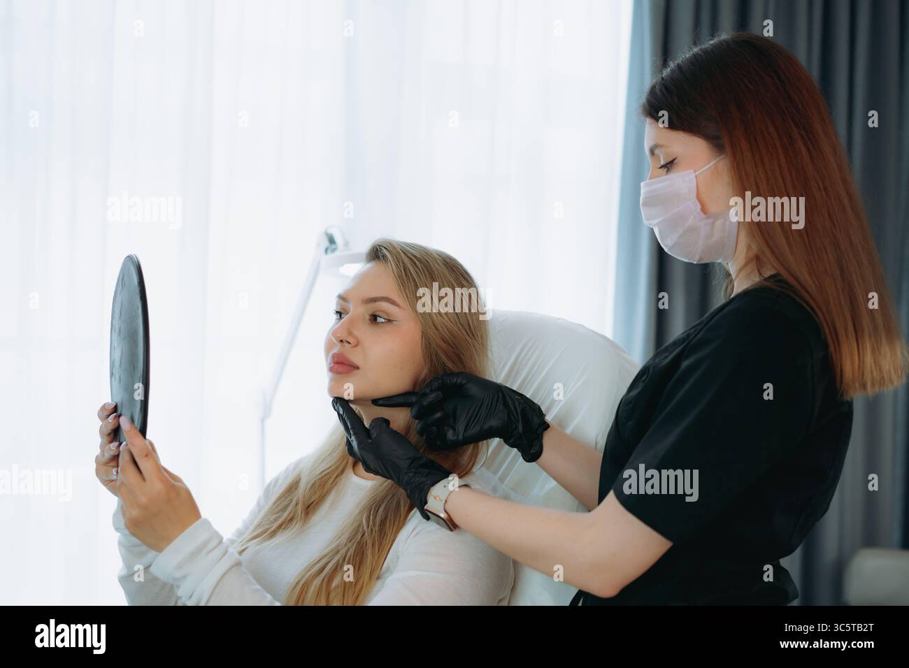 Frau, die in einen Spiegel schaut nach Faziumverjüngung in der ästhetischen Klinik Stockfoto