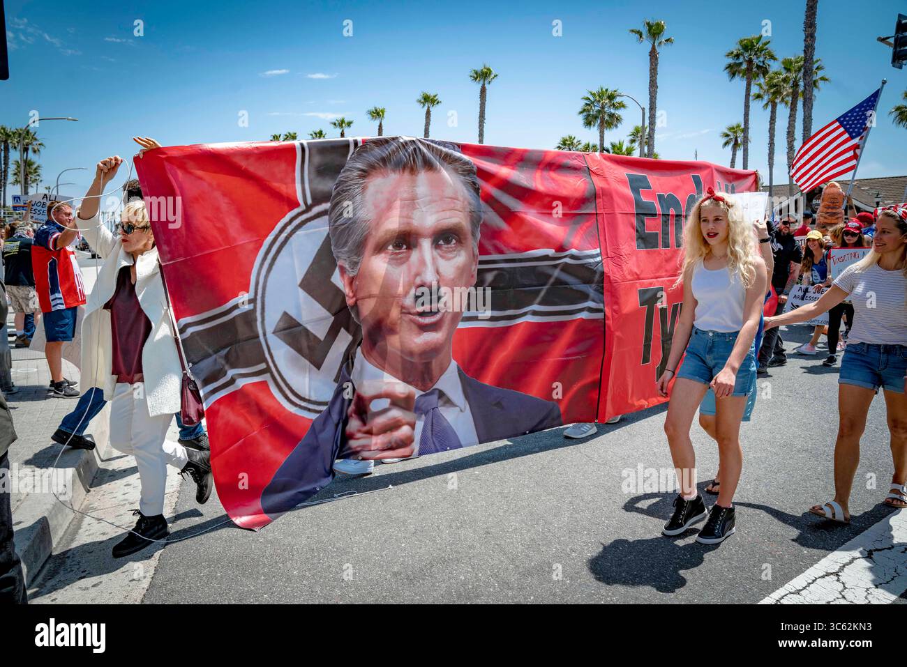 9. Mai 2020, Huntington Beach, Kalifornien, USA: Demonstranten tragen durch die Kreuzung ein großes Banner, das den Gouverneur mit einem bemalten Hitlerbart zeigt. Der rechte Aktivist Leigh Dundas führt die Anklage an. Während eines Reopen California Protests in der Nähe des Huntington Beach Pier. (Kreditbild: © Orin Louis/ZUMA Wire) Stockfoto