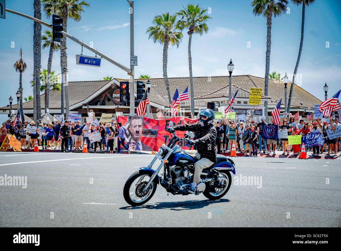 9. Mai 2020, Huntington Beach, Kalifornien, USA: Ein Motorradfahrer biegt die Ecke vor einem großen Banner ab, das den Gouverneur mit gemaltem Hitlerbart zeigt. Während eines Reopen California Protests in der Nähe des Huntington Beach Pier. (Kreditbild: © Orin Louis/ZUMA Wire) Stockfoto
