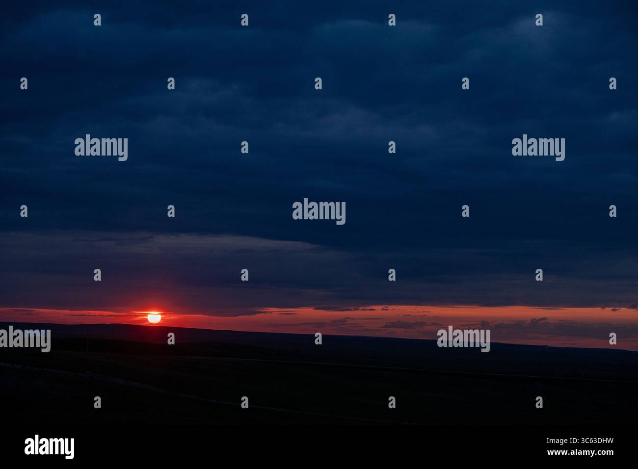 Der Sonnenuntergang gleitet unter dunklen Sturmwolken über den Ebenen von South Dakota und wirft goldenes Licht über die weite Prärie unter einem dramatischen Abendhimmel. Stockfoto