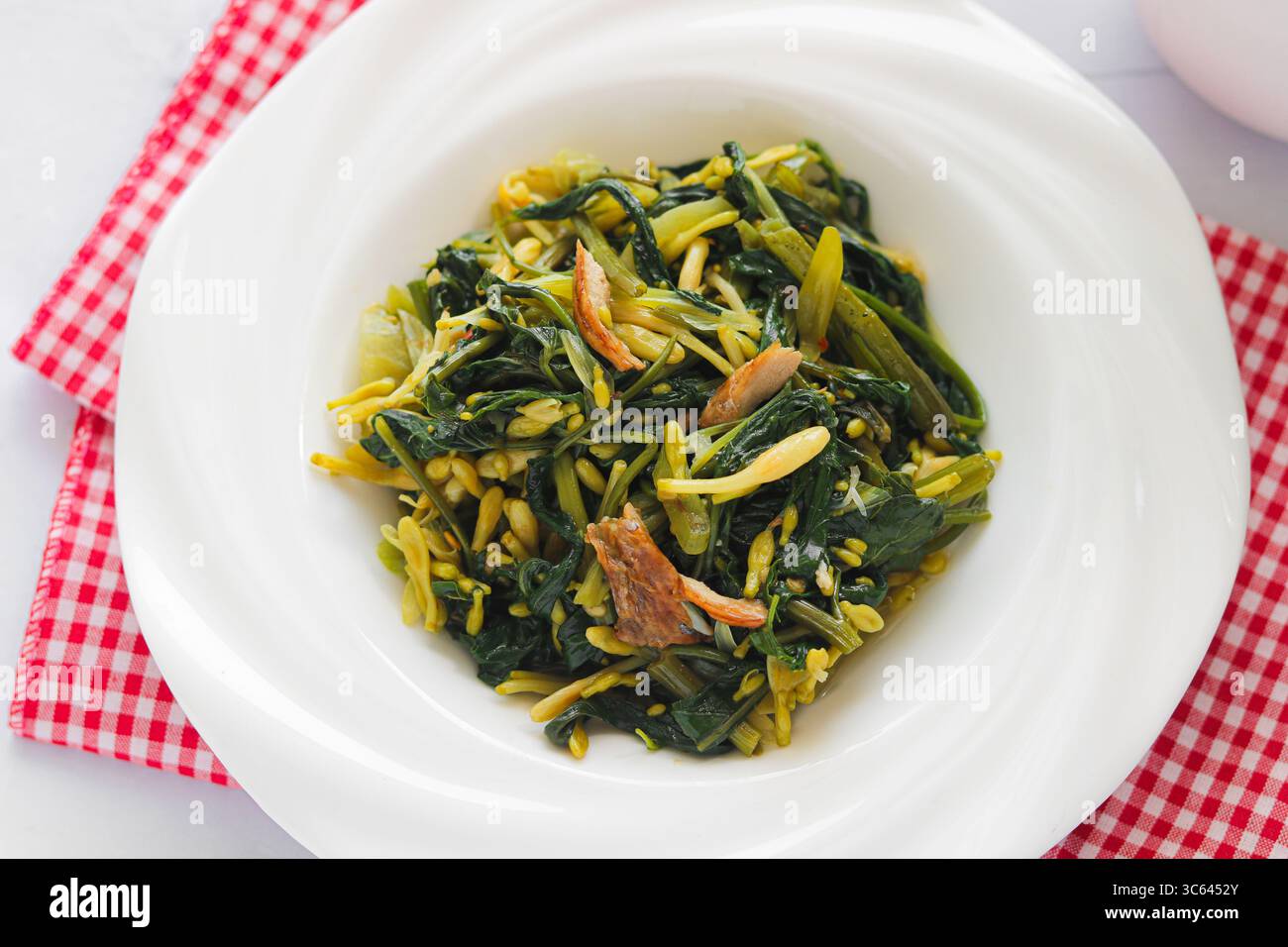 Nahaufnahme eines Tellers mit gebratenem Gemüse im Manado-Stil (Kangkung Bunga Pepaya) mit frischen, belaubten Zutaten und aromatischen Gewürzen. Stockfoto