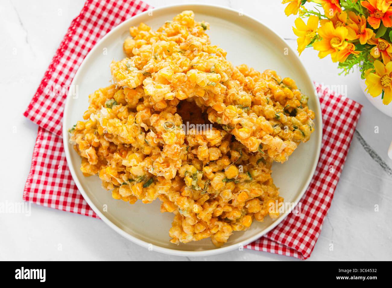 Eine Portion frisch gebratener Corn Fritters (Bakwan Jagung), Golden und knusprig, serviert auf einem weißen Teller mit einem karierten Tuch. Stockfoto