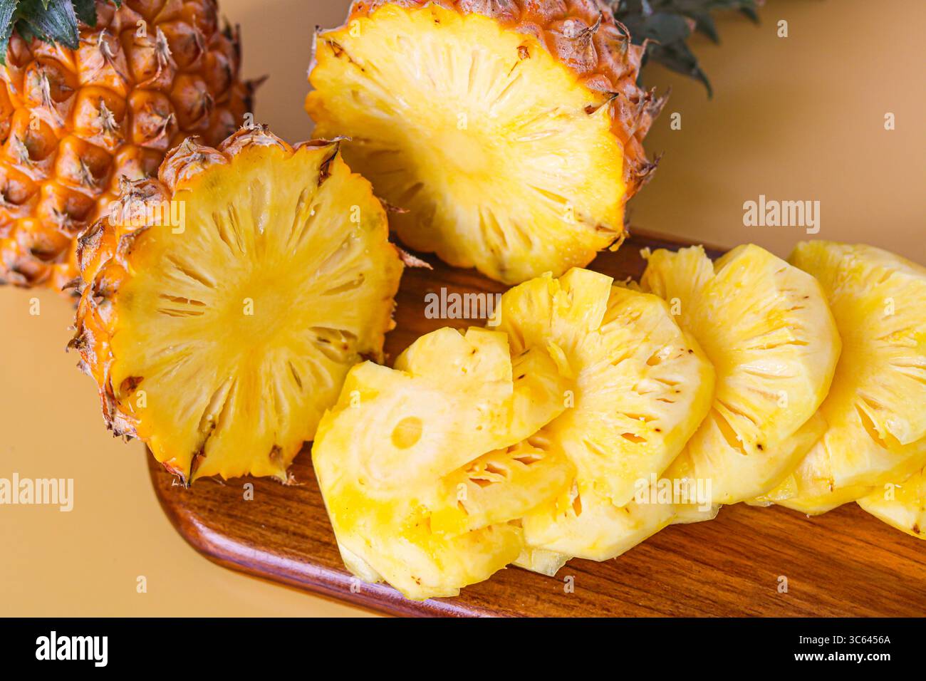 Nahaufnahme einer frisch geschnittenen Ananas auf einem hölzernen Schneidebrett, hinter der eine ganze Ananas steht für eine lebendige tropische Präsentation. Stockfoto
