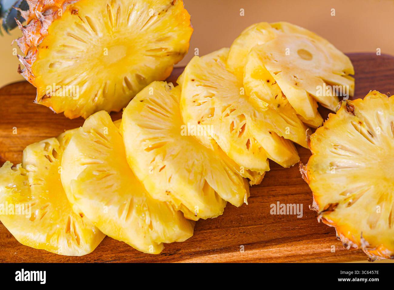 Frisch geschnittene Ananasscheiben, kunstvoll auf einem Holzschneidebrett angeordnet, sorgen für eine lebendige tropische Präsentation. Stockfoto