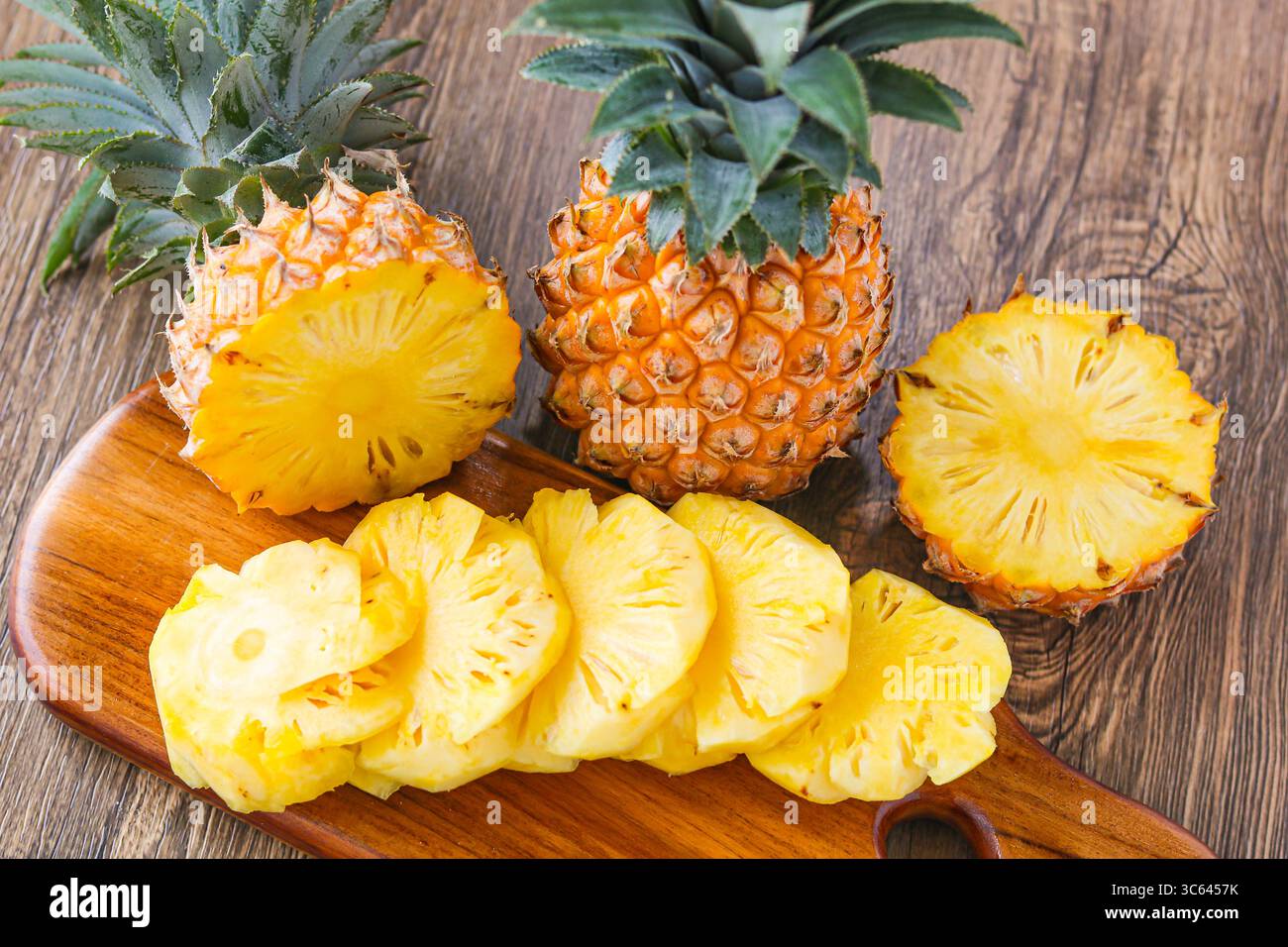 Frisch geschnittene Ananas auf einem hölzernen Schneidebrett angeordnet, mit einer ganzen Ananas dahinter für eine lebendige tropische Präsentation. Stockfoto