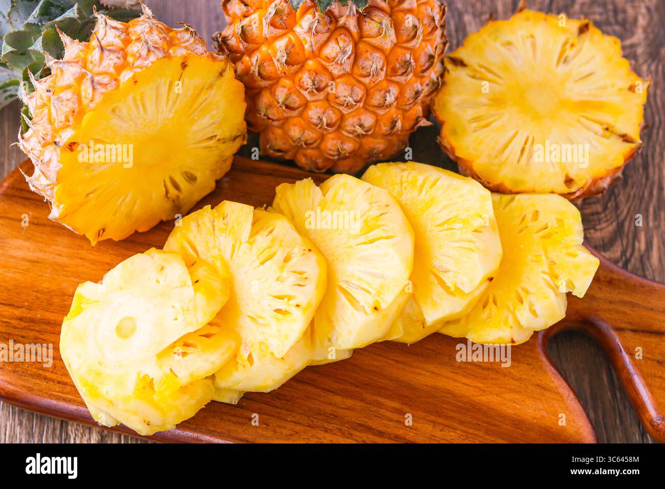 Nahaufnahme der frisch geschnittenen Ananas auf einem hölzernen Schneidebrett, mit einer ganzen Ananas hinter der Tür für eine lebendige tropische Präsentation. Stockfoto