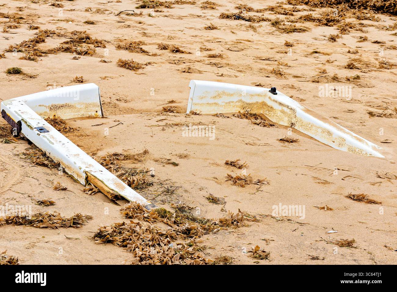 Die verwitterten Überreste eines gebrochenen weißen Bootsrahmens, teilweise in goldenem Sand vergraben. Stockfoto