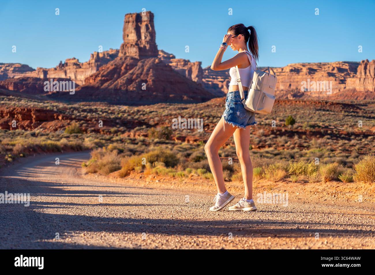 Eine Frau läuft gemächlich auf einem staubigen Feldweg in der weiten Wüste. Junge Frau auf der Straße im Tal der Götter Stockfoto