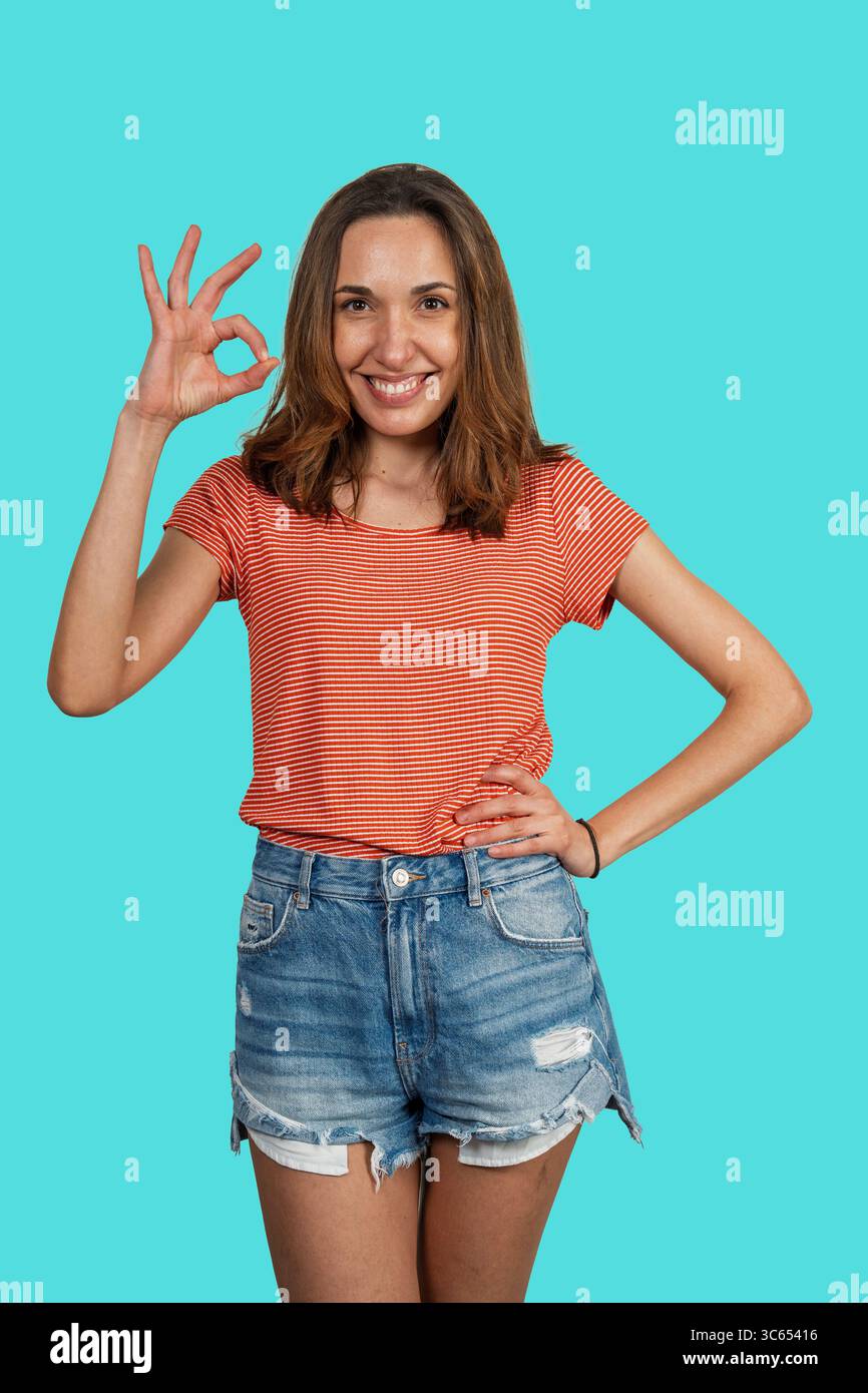 Porträt einer glücklichen lässigen Frau, die mit den Fingern ein OK-Zeichen mit Gesten drückt, lächelt und Positivität auf türkisfarbenem Hintergrund ausdrückt Stockfoto