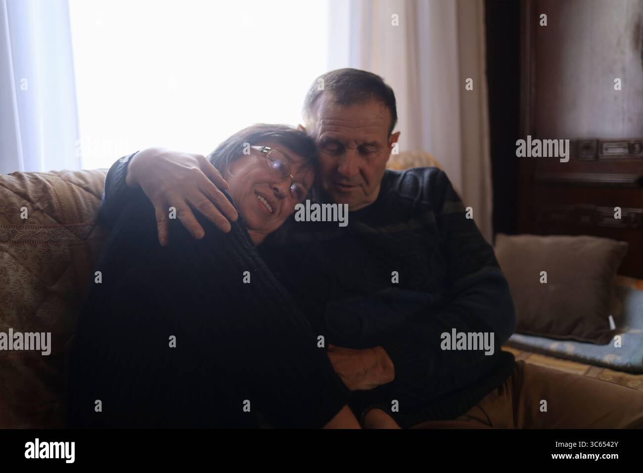 Ein älterer Mann umarmt seine ältere Frau in ihrem Haus. Stockfoto