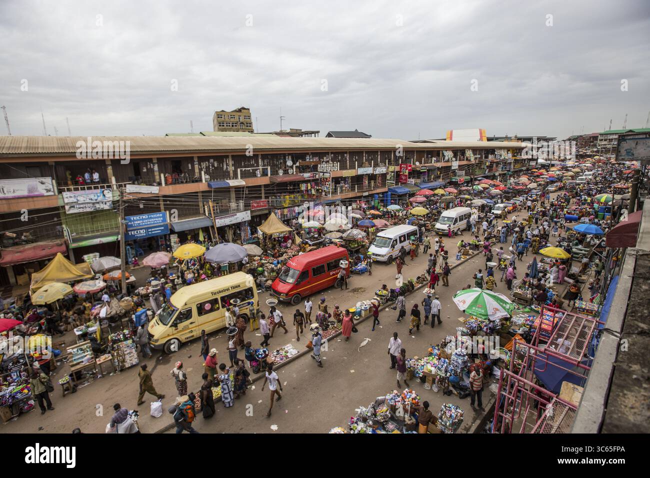 Tafo, Ghana - 26. Mai 2017: Aus der Vogelperspektive auf einen belebten Marktplatz mit leuchtenden Regenschirmen, die sich vom stumpfsinnigen Himmel und den überfüllten Straßen abheben. Stockfoto